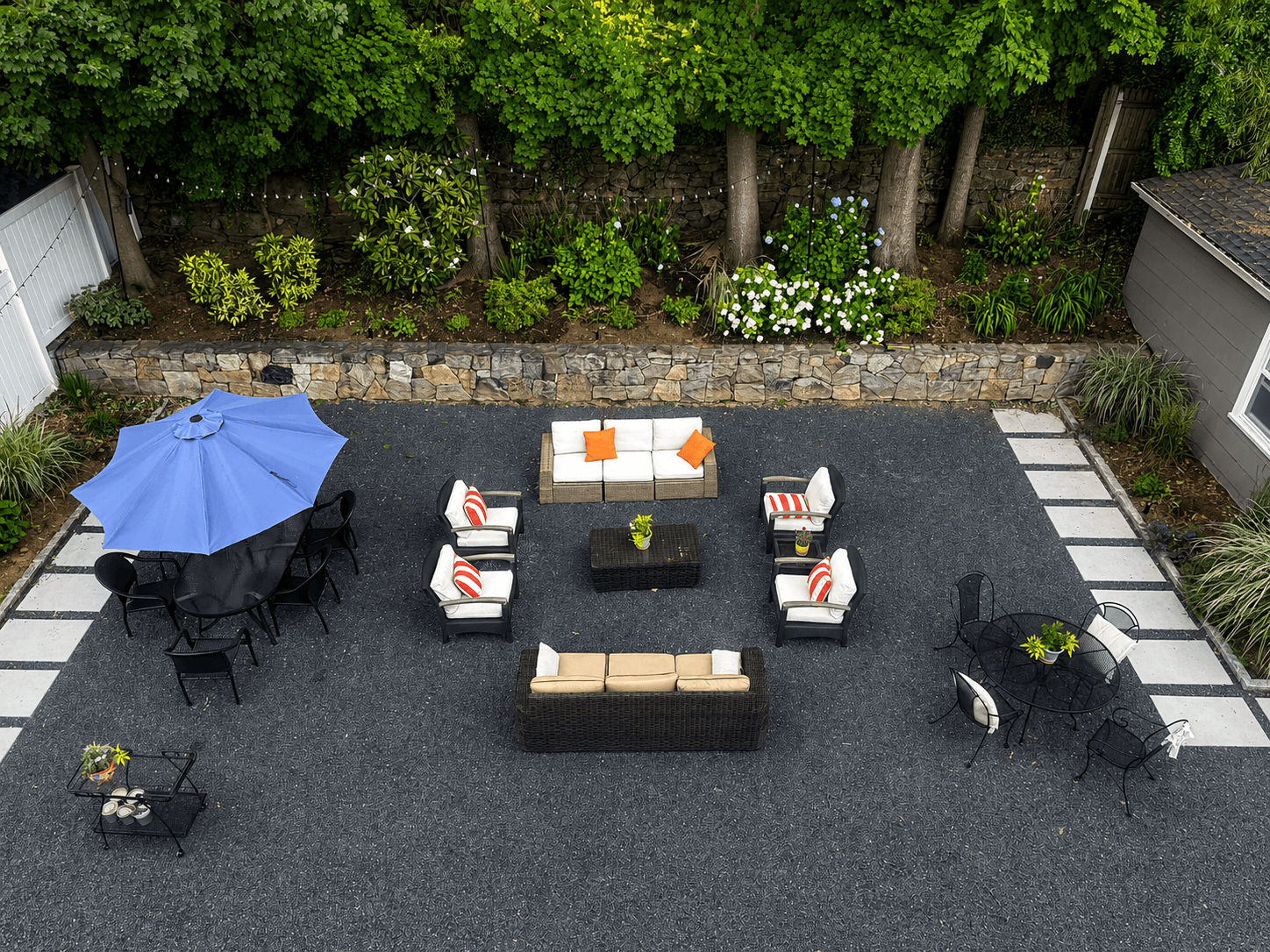 Finished backyard patio in dark gravel bordered by stone pavers, with two seating areas under a blue umbrella